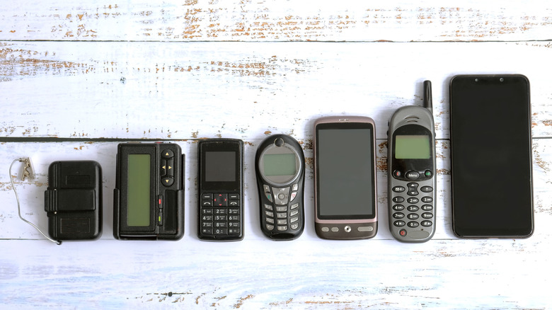 Old pagers and phones lined up on wooden table alongside a modern smartphone