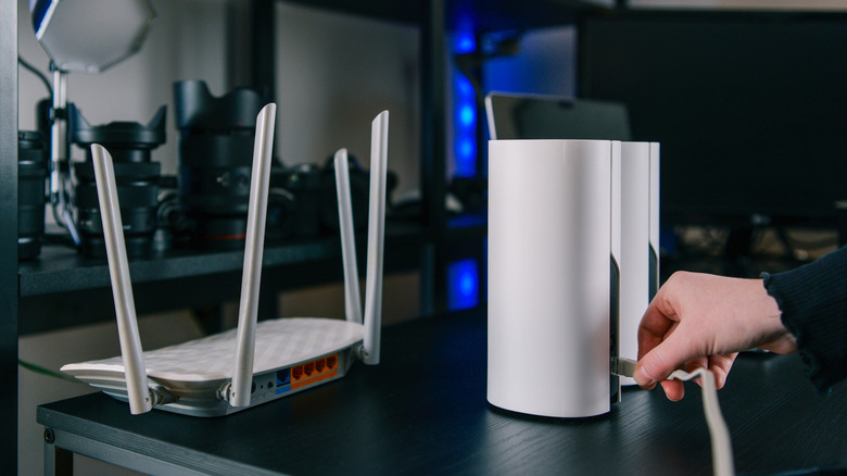 A person's hand plugging an Ethernet cable into mesh networking nodes next to a central router