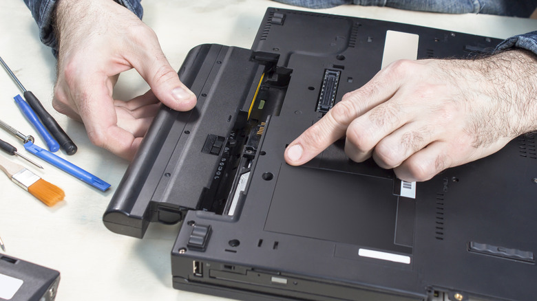 A technician replacing a laptop's battery, with necessary tools and a brush on the same table