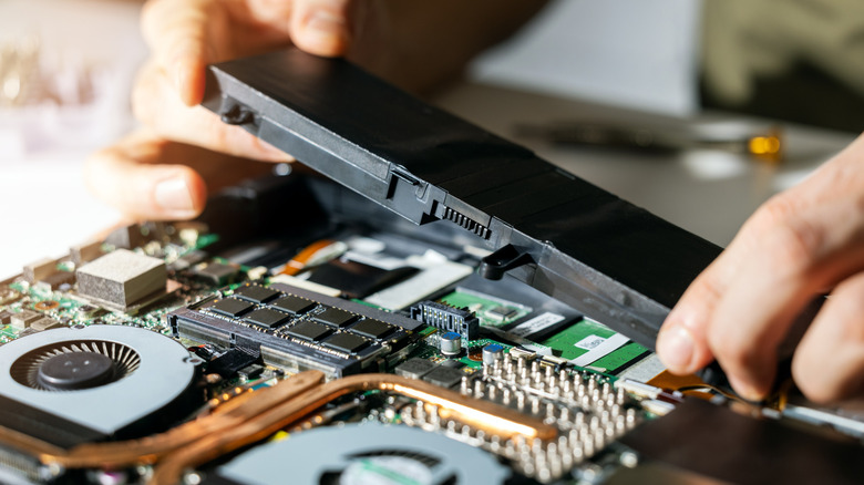 A person removing the battery from a laptop with the internal components visible