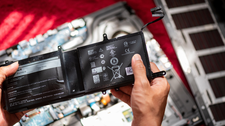 A person holding a swollen laptop battery over a disassembled laptop