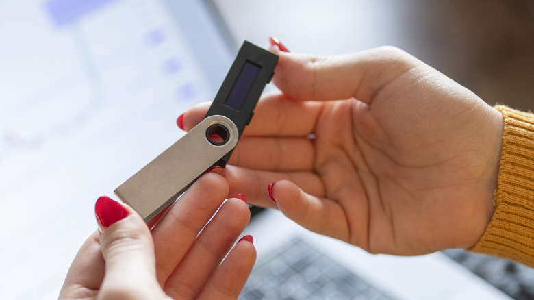 A person holding a USB flash drive in front of an open laptop.