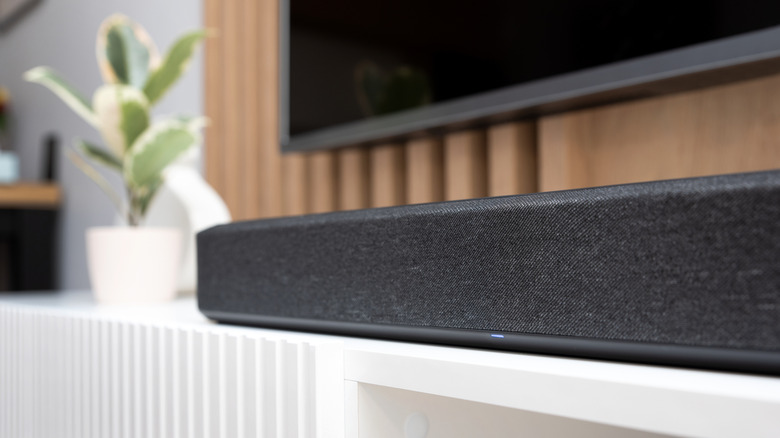 A soundbar placed on a white surface below a TV