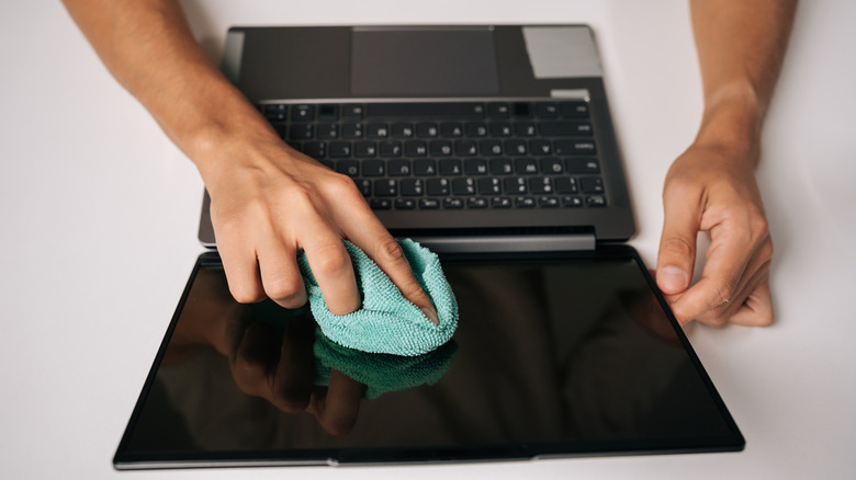 A person cleaning a laptop screen with a microfiber cloth.