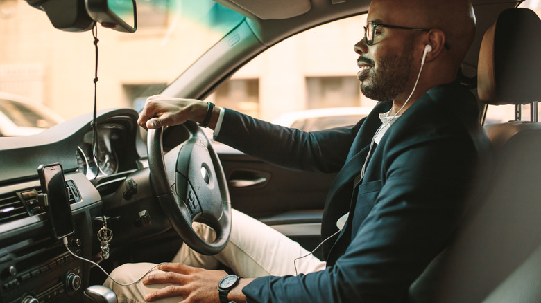 A man in a suit driving while wearing a wired earbud.
