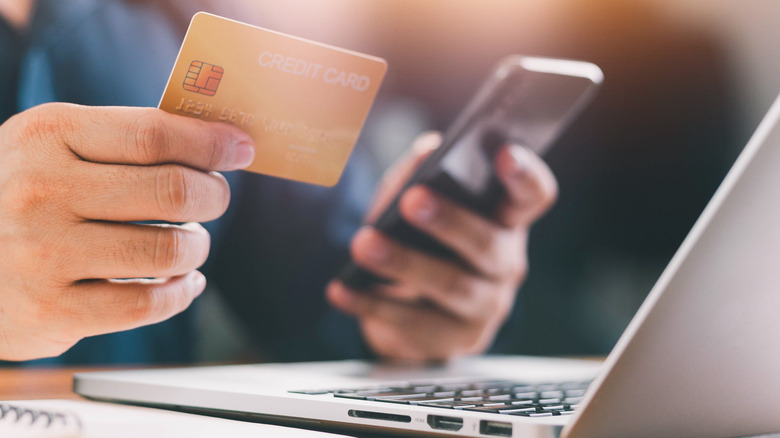 person holding credit card and phone by laptop