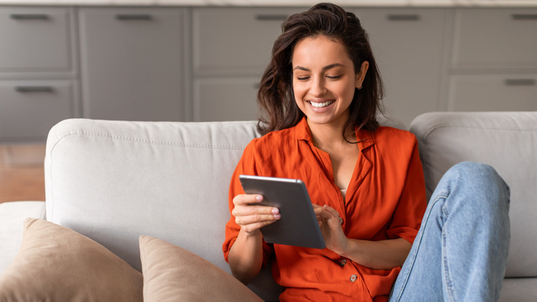 Woman on the couch smiling holding a tablet.