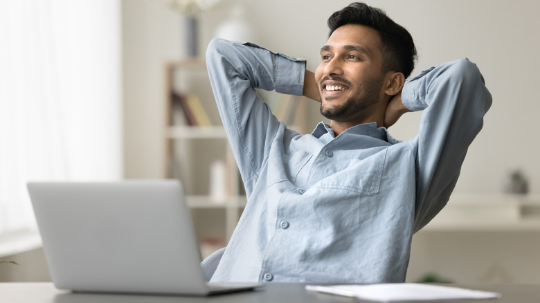 Man leaning back, arms behind his head smiling in front of a laptop.