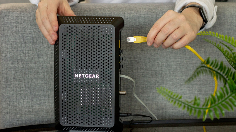 A hand plugging in Ethernet cable to Netgear router