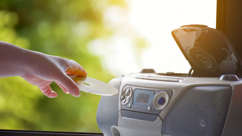 A hand putting a CD into a boombox.