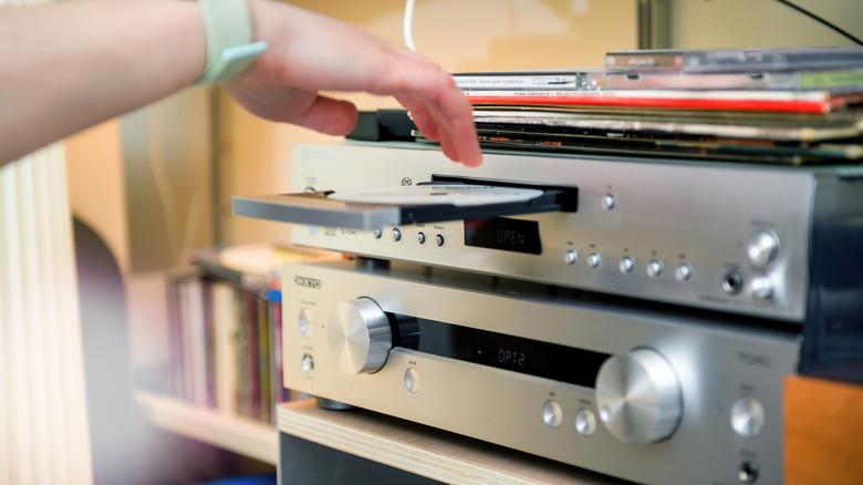 A hand putting a CD into the tray of a CD player.
