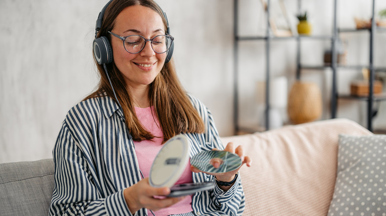 A woman putting a CD into a portable CD player while wearing headphones.