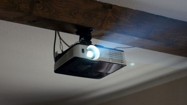 Ceiling-mounted projector casting light from under a wooden beam.