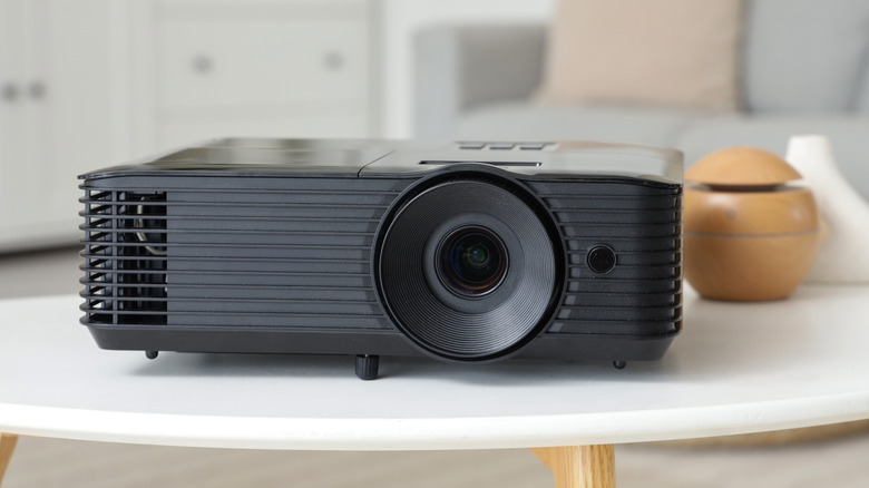 Black projector sitting on a white table in a living room.
