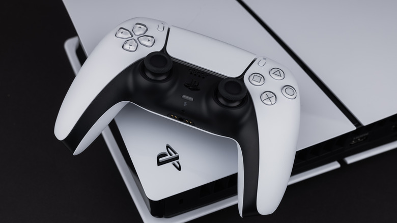 A PS5 dualsense controller sitting on top of the PS5 console on a black background