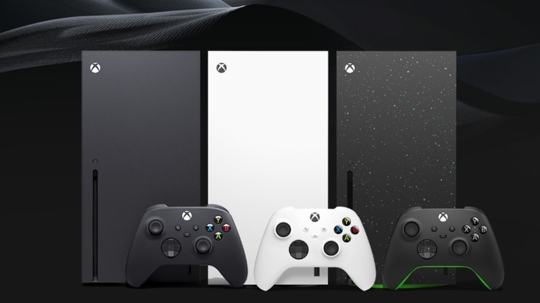 Black, white, and black and green Xbox Series X consoles on a black background with matching controllers in front of them