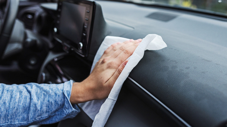 A person using a piece of paper towel to clean a car dashboard.