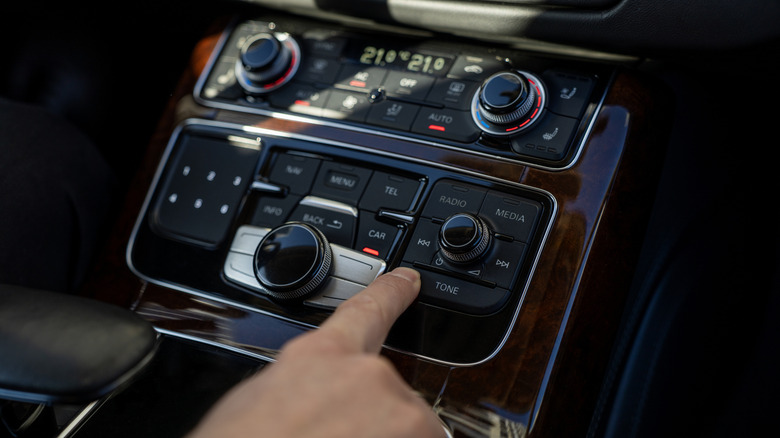 A driver pressing the tone button on a car infotainment system to adjust EQ settings.