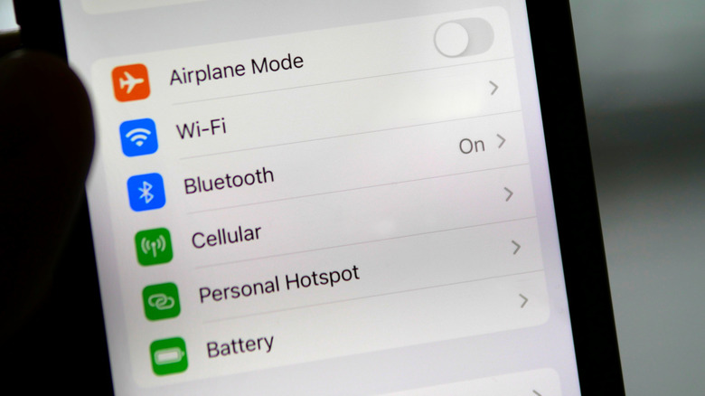 A hand holding an iPhone displaying the settings screen showing a menu item for battery management