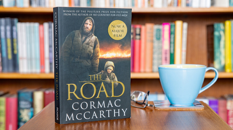 A copy of The Road by Cormac McCarthy with the film tie-in cover on a table in front of a bookshelf
