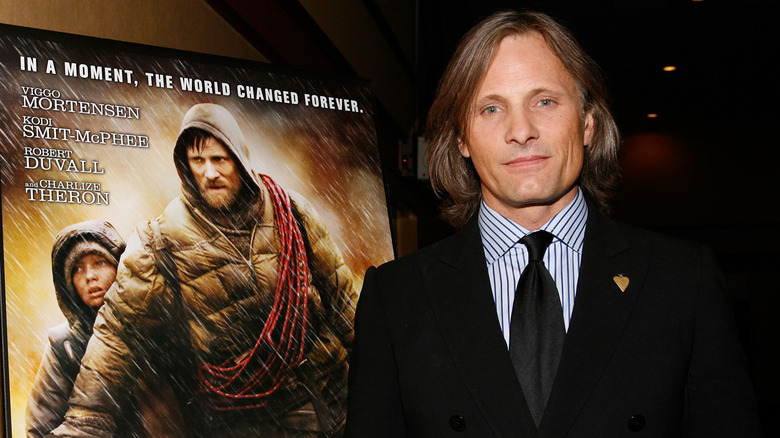 Viggo Mortensen standing in front of a film poster for The Road