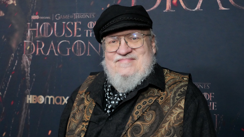 George RR Martin stands before a poster for the new Game of Thrones television series, House of the Dragon.