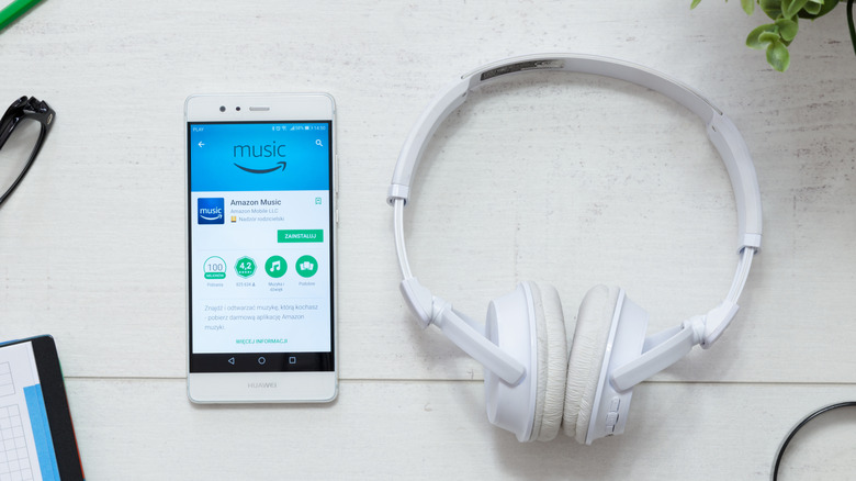 A pair of Amazon earbuds, next to a phone showing the Amazon Music app.