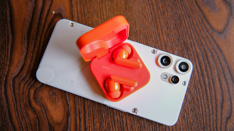 A pair of CMF earbuds, leaning on a CMF smartphone.