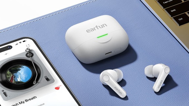 A pair of Earfun earbuds next to a smartphone and keyboard.