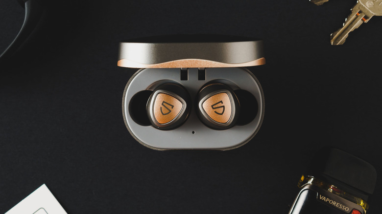 A pair of Soundpeats earbuds, in their charging case and on a black backdrop.