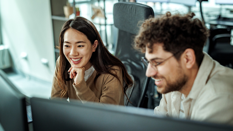 Two people sitting at a desk in front of PC monitors