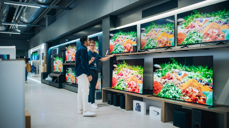 An electronic store employee showing TV options to a customer.