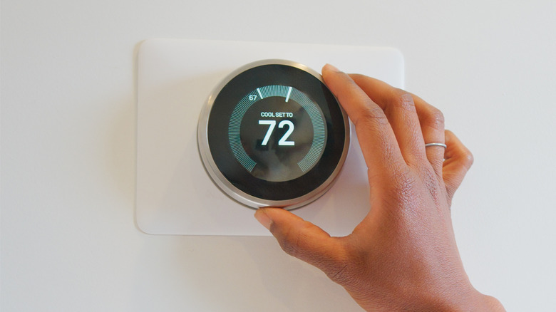 A person manually adjusting the temperature of a smart thermostat.
