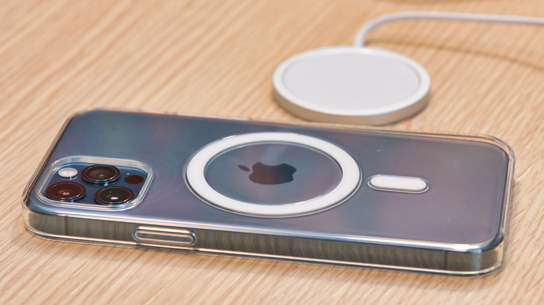 An iPhone 12 in a clear MagSafe charging case sitting next to a MagSafe charging puck, both items are laying on a table
