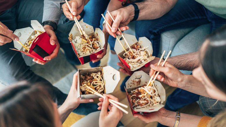 A top down photo of five people eating takeout noodles together