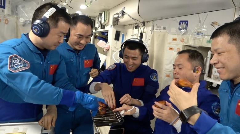 A group of astronauts enjoy their dinner of chicken wings aboard the Tiangong Space Station.