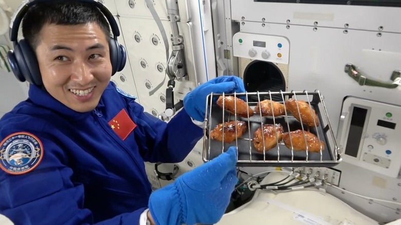 An astronaut pulls out a tray of fully baked chicken wings out of the Tiangong's new space oven.