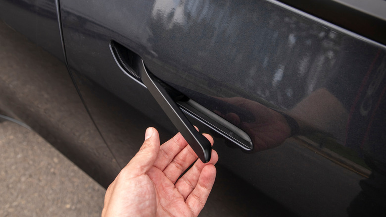 The left hand of an individual as it pulls on a vehicle's black doorhandle, the handle was recessed into the vehicle