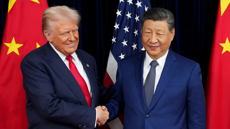 American President Donald Trump and Chinese President Xi Jinping shake hands before a set of U.S. and Chinese flags.