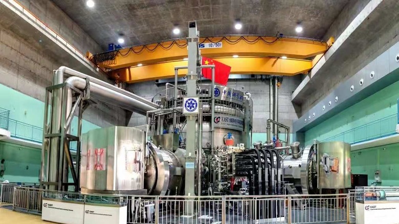 The Experimental Advanced Superconducting Tokamak is a tall silver cylinder surrounded by pumps and industrial machinery.