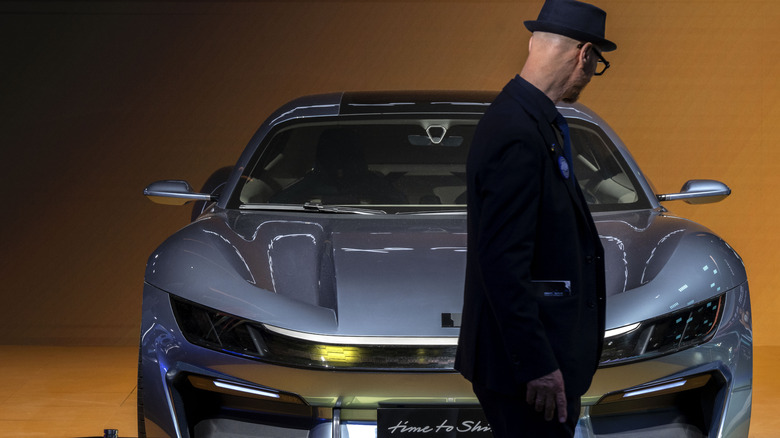 A man in a black coat and hat looking at a silver electric sports car by Lynk & Co, a division of Geely, at Auto China 2026 in Beijing.