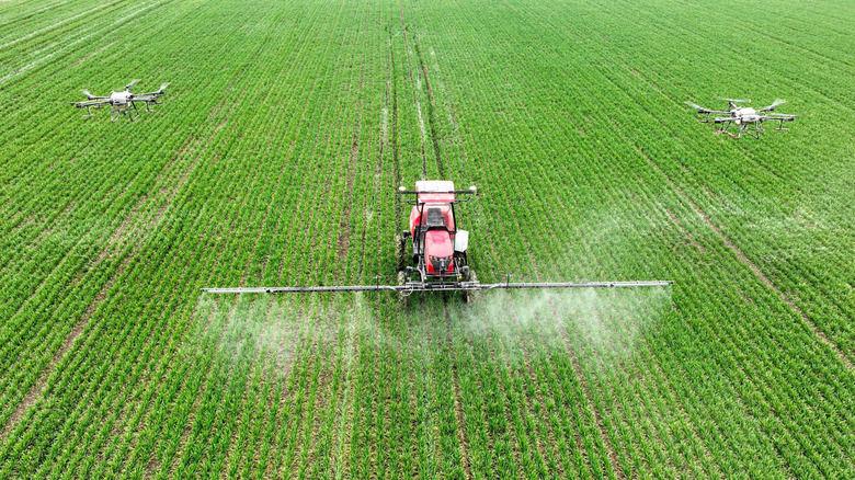 Two unmanned drones and a red tractor against a vast green farm field