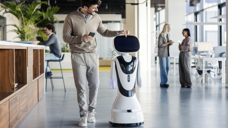 Man walking alongside a customer service robot with a screen in an office.