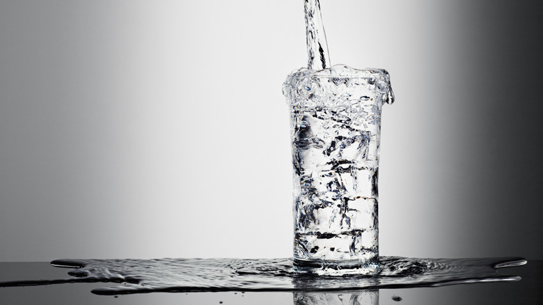 Water being poured into a tall glass that's already overflowing
