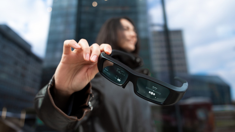A woman holding glasses with an augmented reality user displayed on the lenses interface