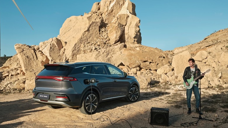 A BYD Tang electric car with a sunroof in the desert next to a person playing an electric guitar