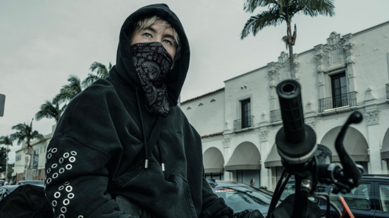 Ormon (Barry Keoghan), masked in a black bandana and hoodie, sits astride a motorcycle against a classic L.A. boulevard