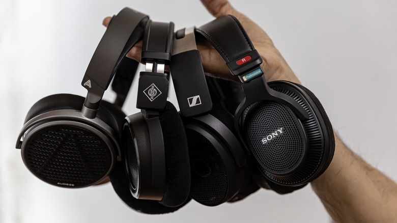 Four pairs of studio-grade open and closed-back headphones hanging in a person's hand.