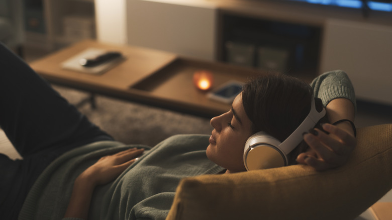 Young woman laying on the couch listening to music with a pair of headphones.