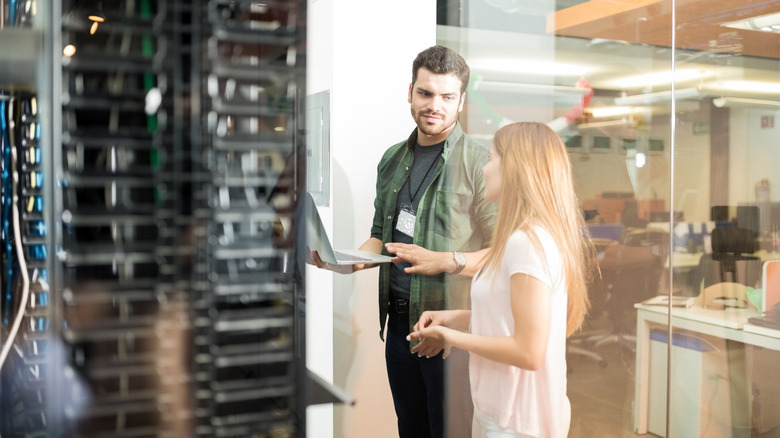 Two people using a laptop near computer servers